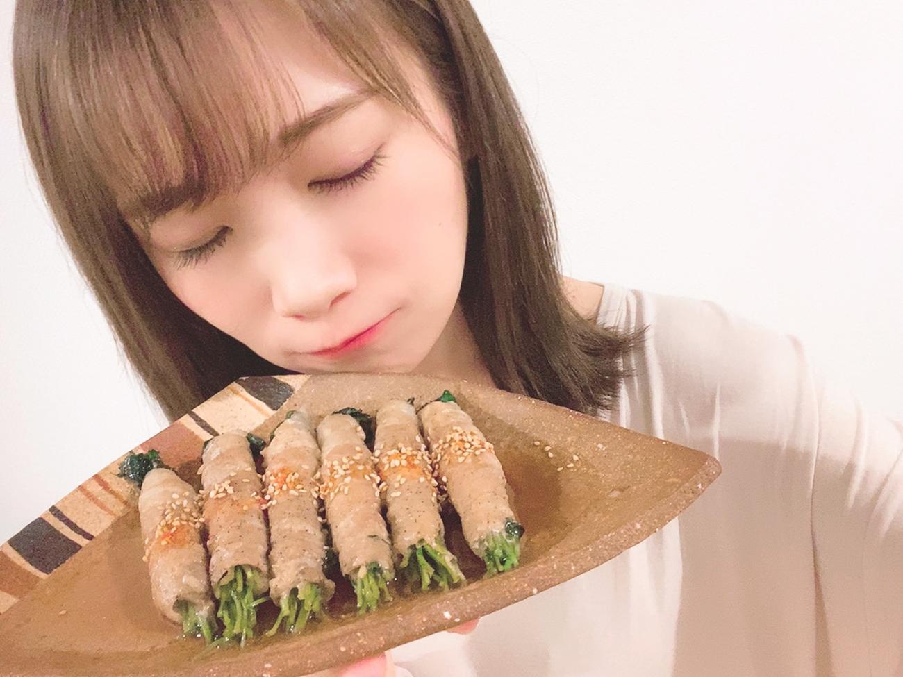 豆苗の豚バラ巻きを持って笑顔を見せる秋元真夏