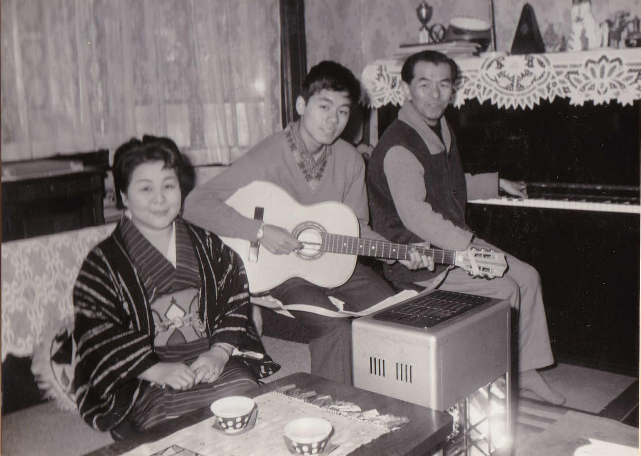 61年、自宅にてギターを抱え、父・古関裕而氏（右）、母金子さん（左）と写真に納まる長男正裕氏（古関正裕氏提供）