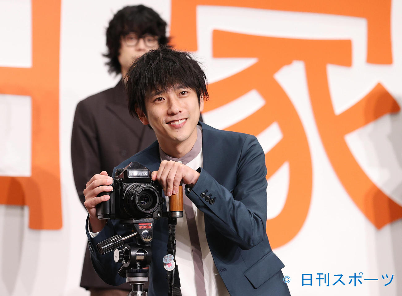 映画「浅田家！」完成報告会でカメラを手に笑顔で写真に応じる二宮和也。後方は菅田将暉（撮影・垰建太）