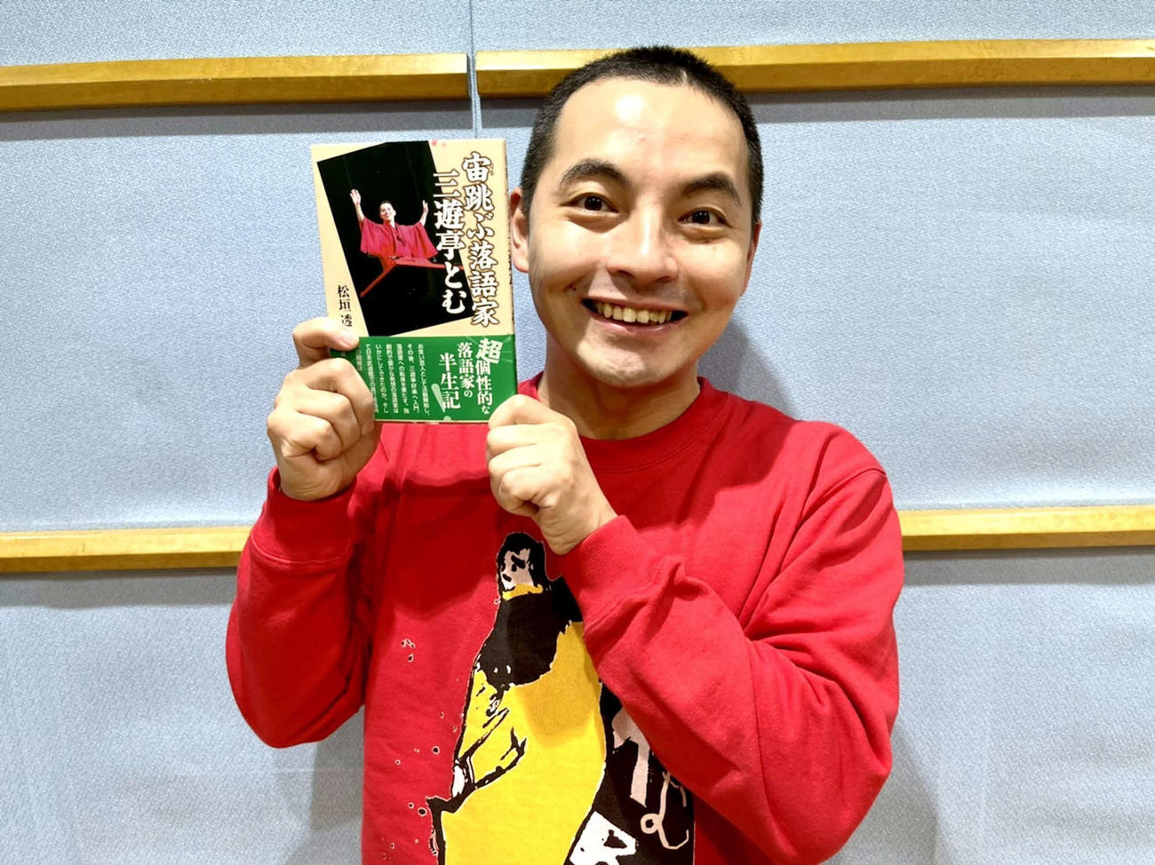 半生をまとめた「宙跳ぶ落語家　三遊亭とむ」を手にする三遊亭とむ