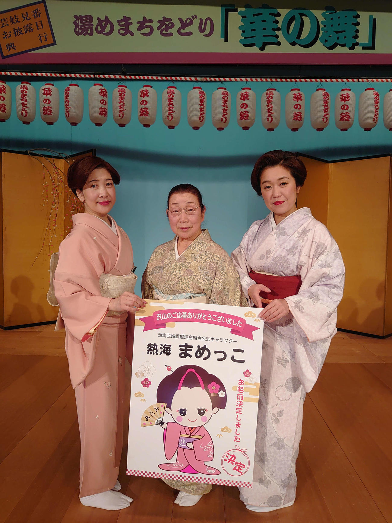 熱海芸妓置屋連合組合の新マスコットキャラクターのポスターを持つ、左から豆一さん、組合長の松千代さん、美保さん