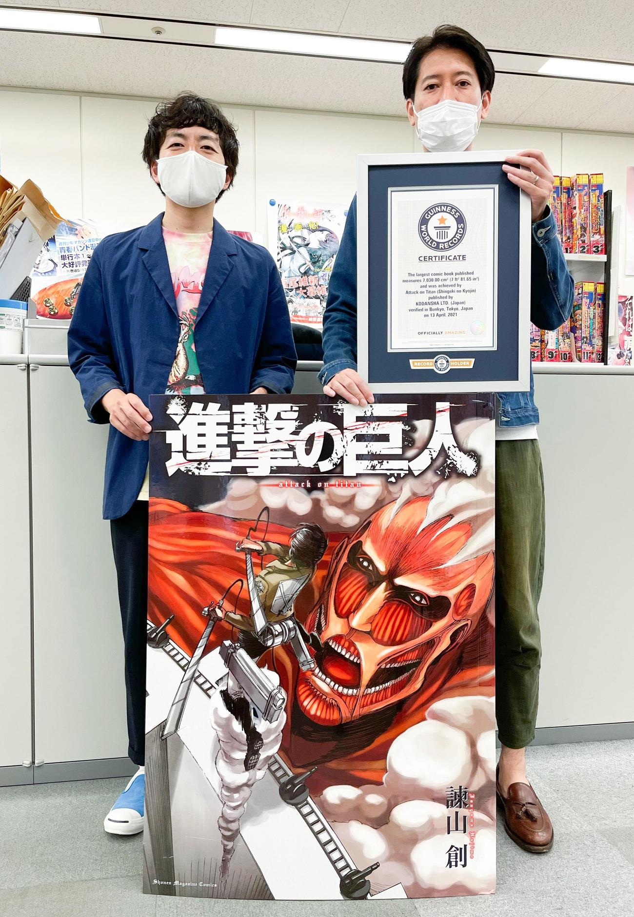 「出版された最大の漫画本」としてギネス世界記録に認定された「巨人用　進撃の巨人」を手にする担当編集の川窪慎太郎氏(左)と宣伝部の田幸志朗氏