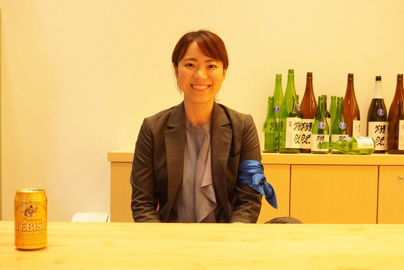 エヴァンゲリオンに登場する「葛城ミサトの部屋」を再現した店内で笑顔を見せる旭酒造広報の千原英梨さん