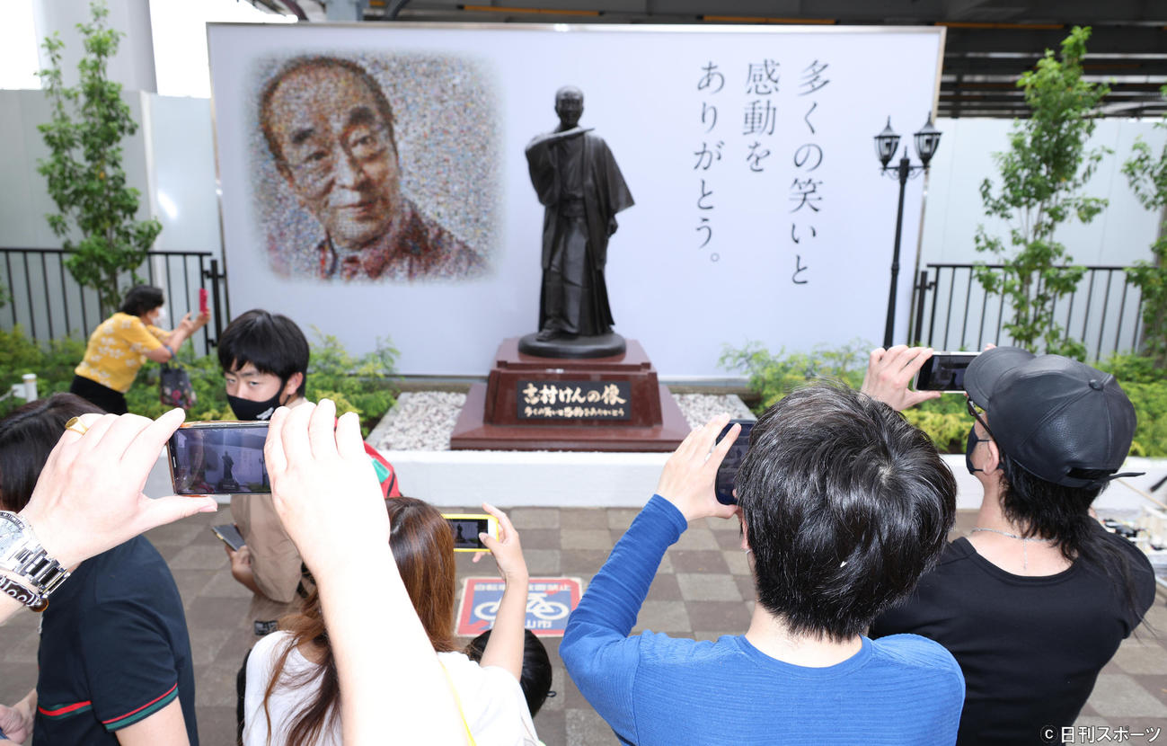 志村けんさんの銅像とファンから寄せられた写真によって作られたコラージュの肖像。多くの市民がスマホで撮影していた（撮影・中島郁夫）