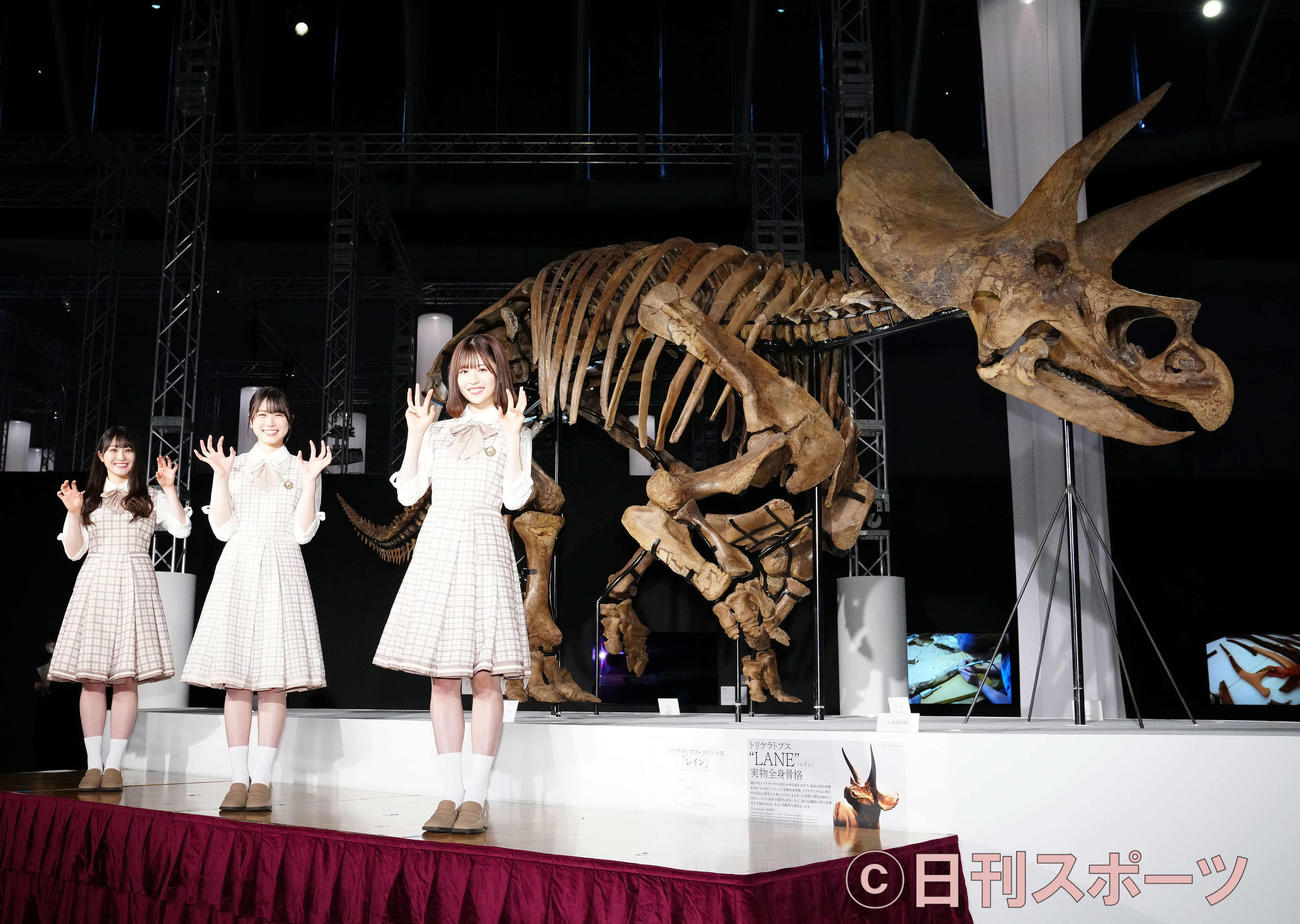 「恐竜科学博」に展示されるトリケラトプスの実物全身骨格「レイン」を背に写真に納まる日向坂46の、左から潮紗理菜、丹生明里、松田好花（撮影・江口和貴）