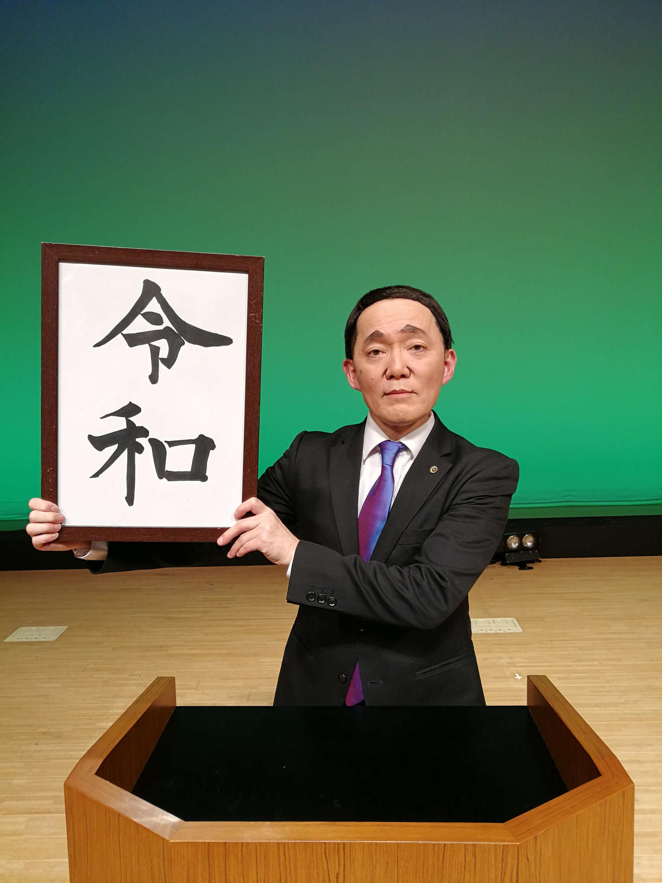 菅義偉首相に扮して「令和」の額を掲げる山本天心（ザ・ニュースペーパー提供）