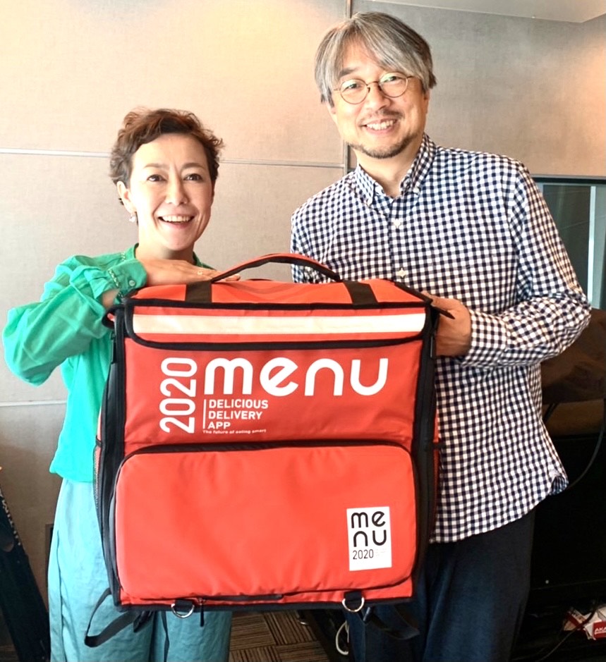夢のコラボを実現した「menu」の配達用バッグをパーソナリティーのクリス智子（左）と持つ小山薫堂氏