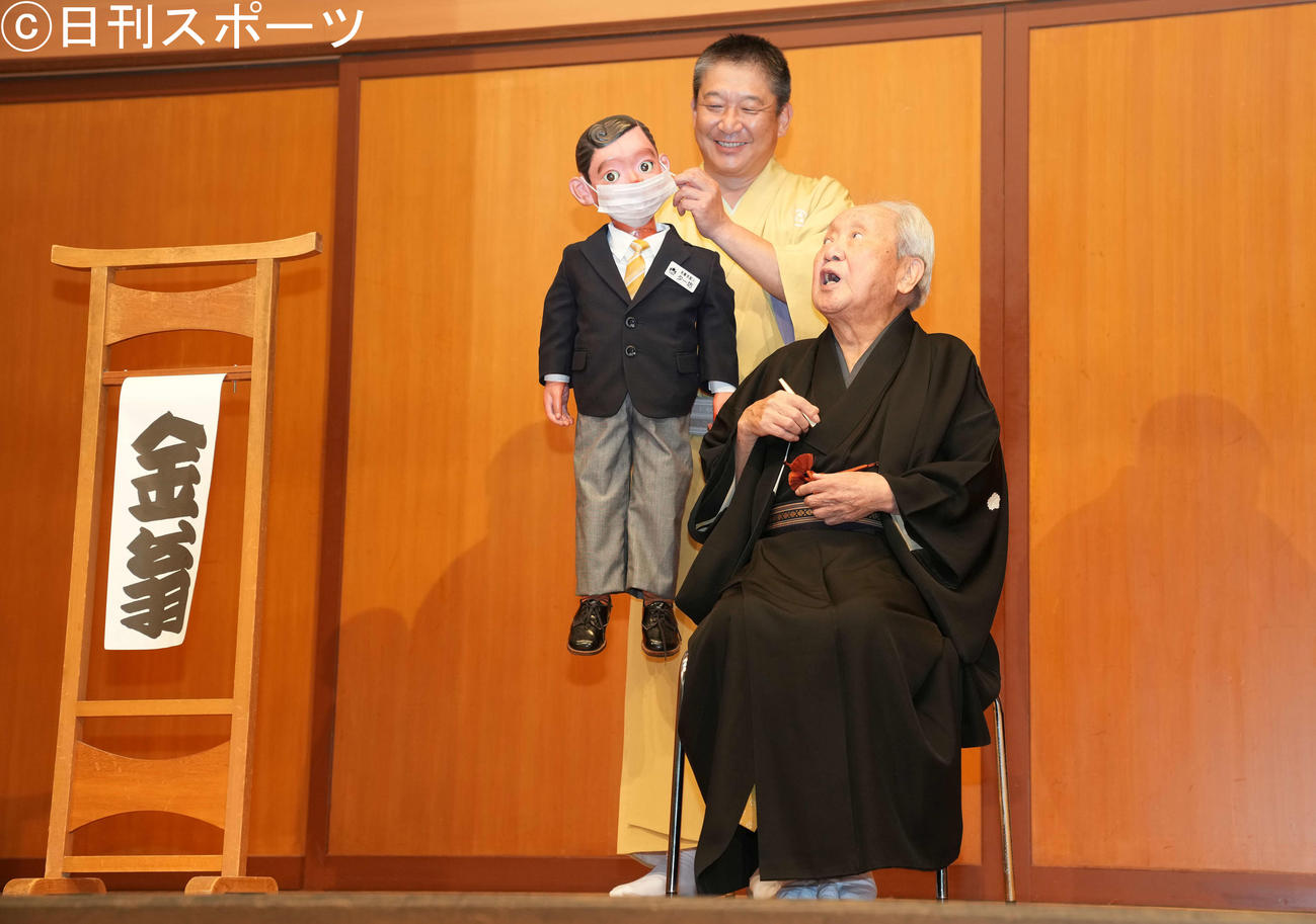 「金翁芸能80周年記念の会～金翁ロードショー～」後の囲み取材で、マスク姿の腹話術人形「ター坊」を見る三遊亭金翁（右）。左は三遊亭金馬（撮影・鈴木みどり）