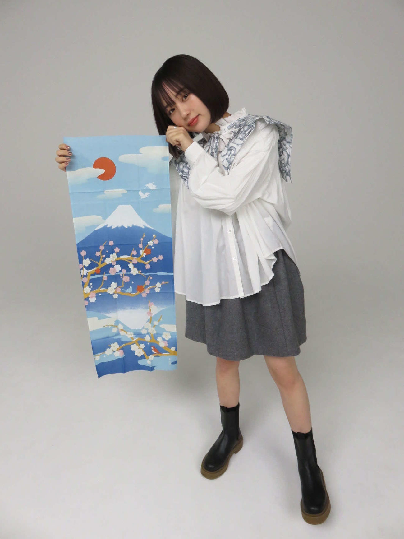富士山の美しさを語ったなえなのは、富士山が描かれた手ぬぐいを広げる