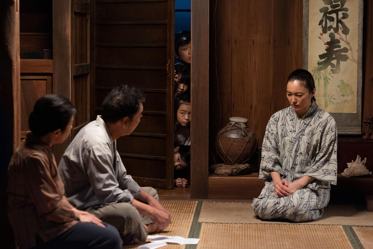 朝ドラ「ちむどんどん」より。親戚と深刻な表情で話す比嘉家の母・優子（仲間由紀恵）とのぞき込む４兄妹（C）NHK