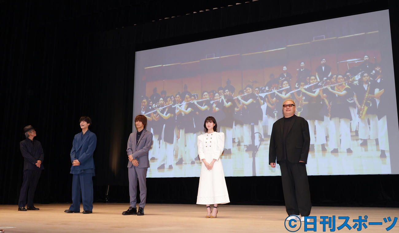 市立船橋吹奏楽部の中継出演を背景に、映画「20歳のソウル」完成披露舞台あいさつを行う、左から佐藤浩市、佐野晶哉、神尾楓珠、福本莉子、秋山純監督（撮影・中島郁夫）