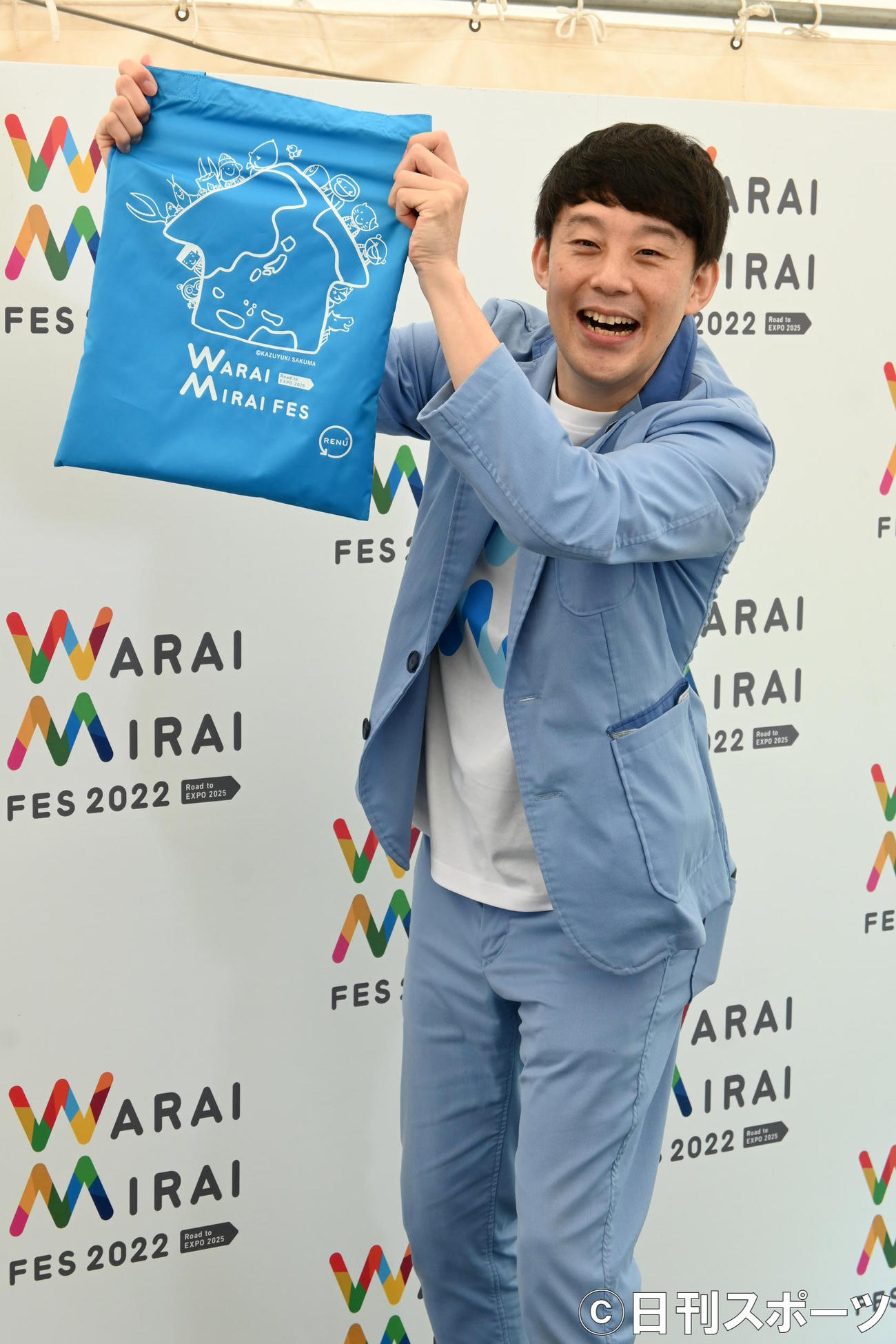 自らが手掛けたイラスト入りのエコバッグを掲げる佐久間一行（撮影・松浦隆司）