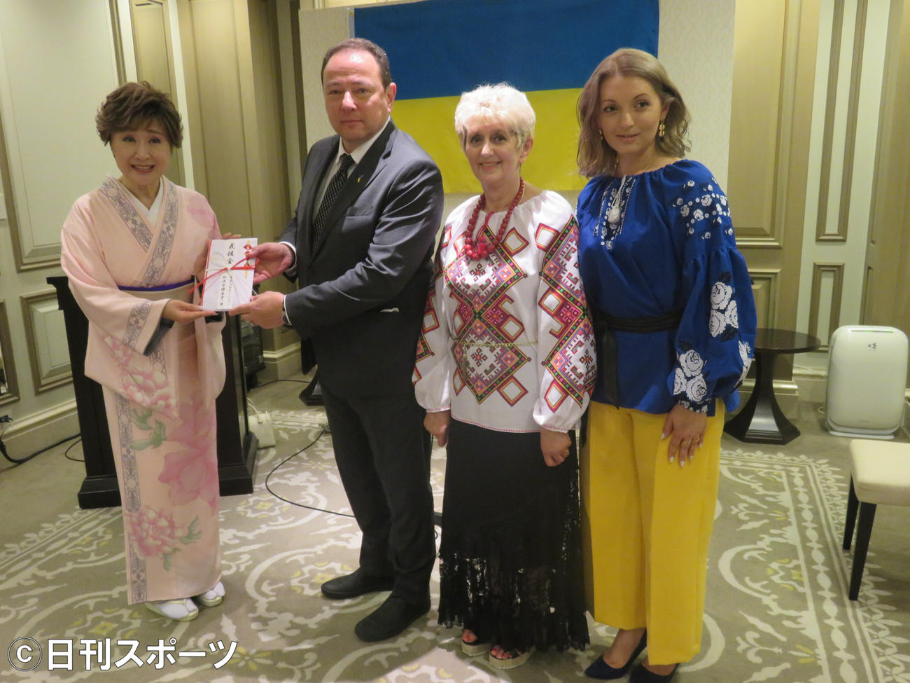 小林幸子（左）はセルギー・コルンスキー駐日ウクライナ大使（左から2人目）に義援金を渡す。ともに写真におさまるカテリーナ（右）と母マリヤさん