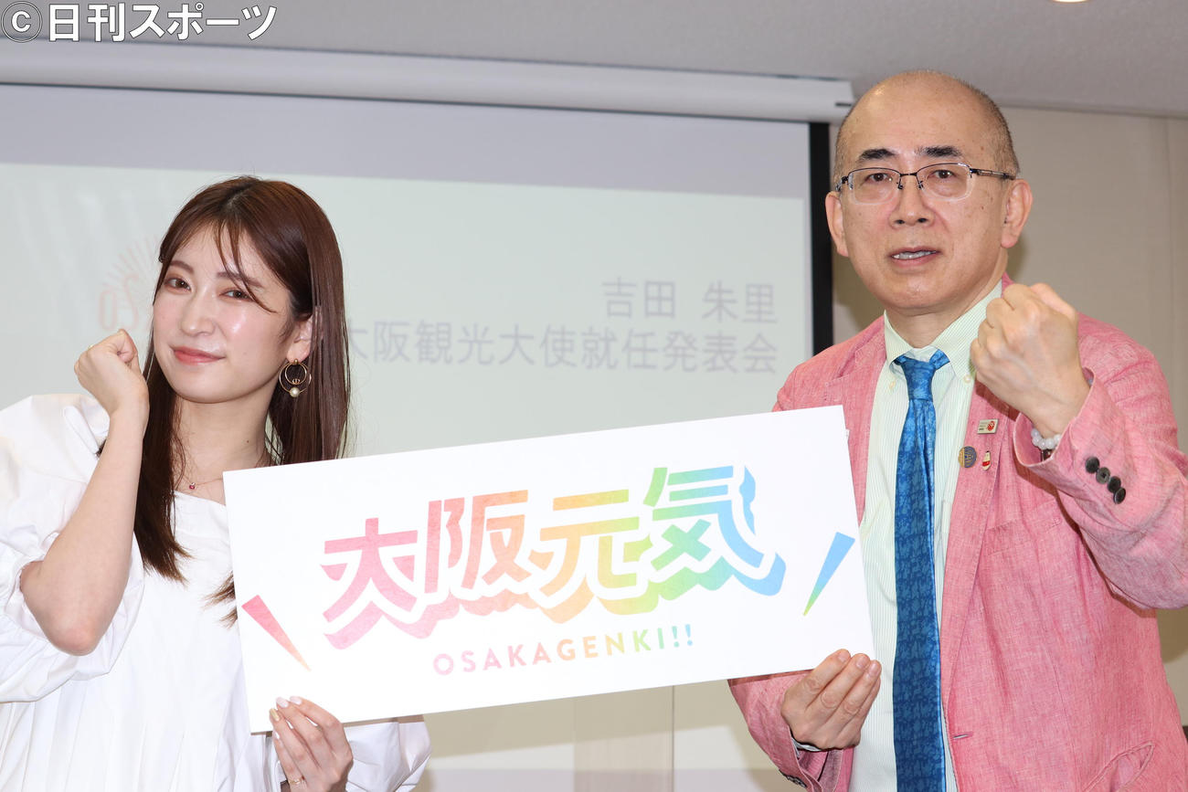 看板を持ち、ガッツポーズをする吉田朱里（左）と溝畑宏大阪観光局理事長（撮影・竹本穂乃加）