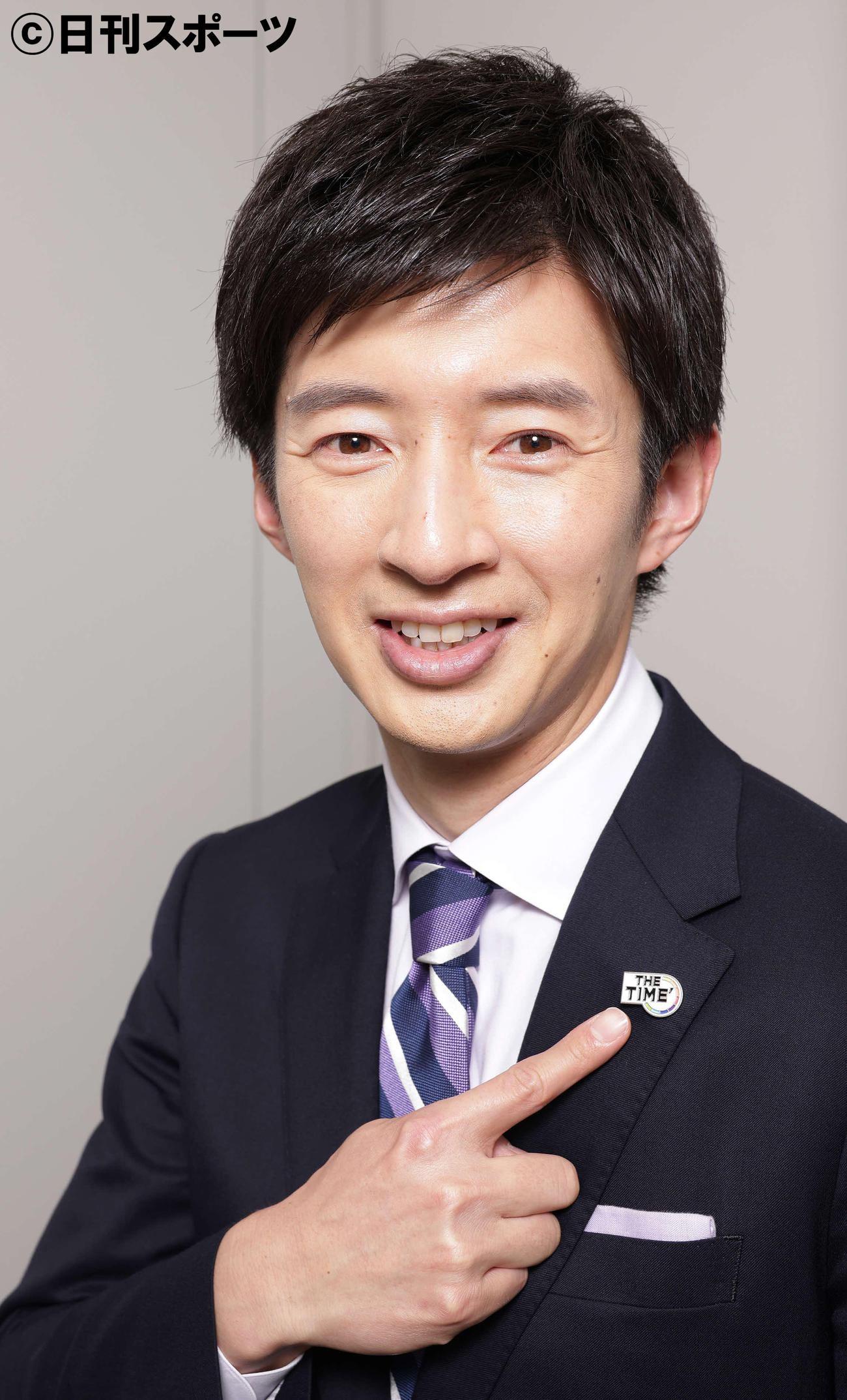 番組ロゴのピンバッジを指さすTBS杉山真也アナウンサー（撮影・中島郁夫）
