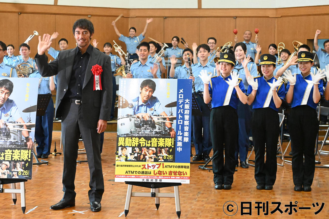 大阪府警察音楽隊と大阪府警察カラーガード隊のメンバーと笑顔で手を振る阿部寛（撮影・松浦隆司）