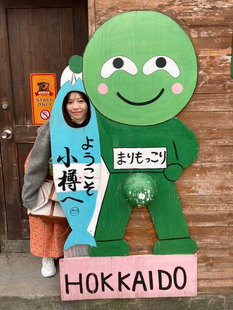 「まりもっこり」のパネルから顔を出す島崎遥香（「私たち結婚しました3」オフィシャルブログより）