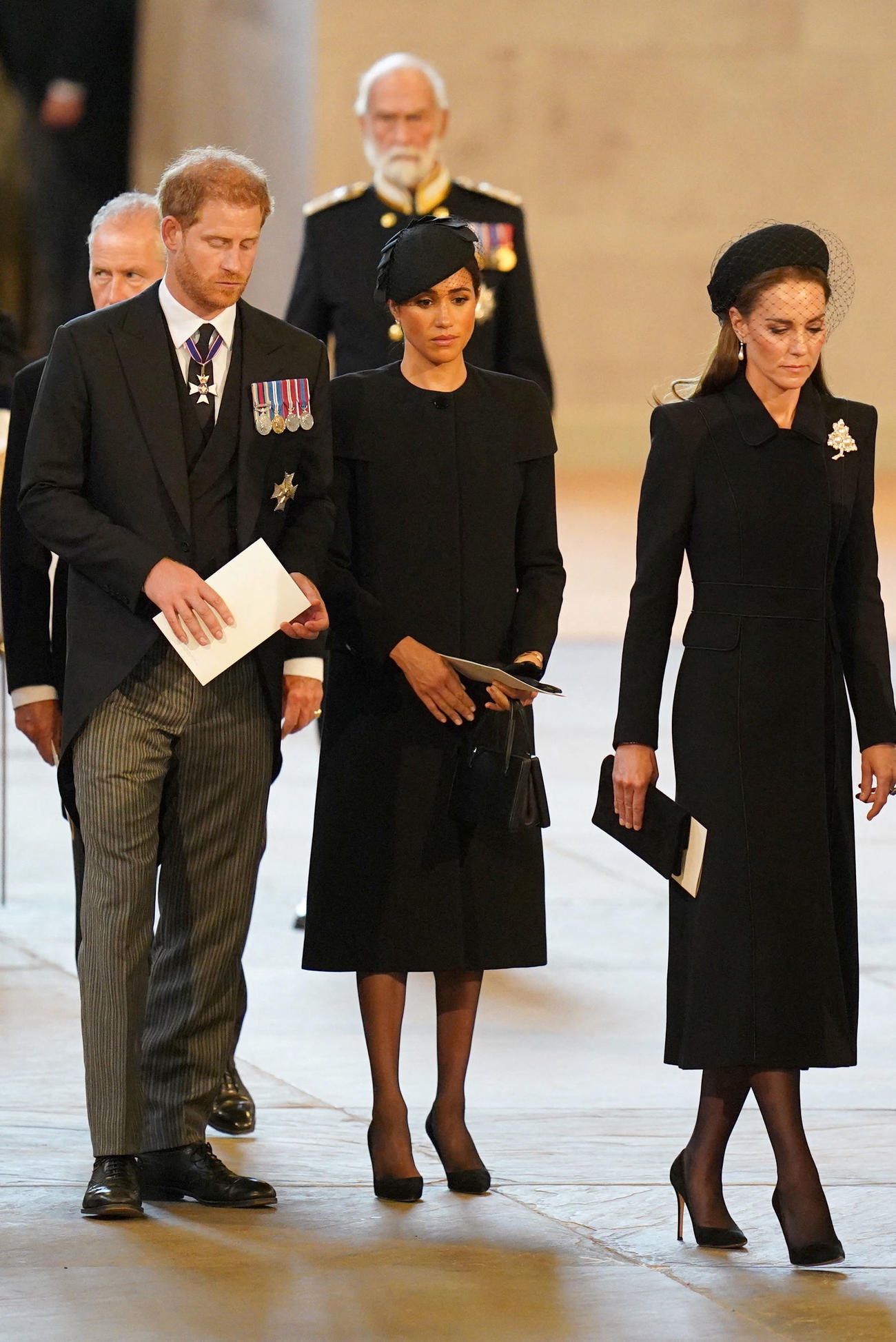 22年9月14日、エリザベス女王のひつぎがウェストミンスター・ホールに運ばれた際に、モーニングスーツの礼服で葬列に加わったヘンリー王子（左）。中央は妻のメーガン妃（ロイター）