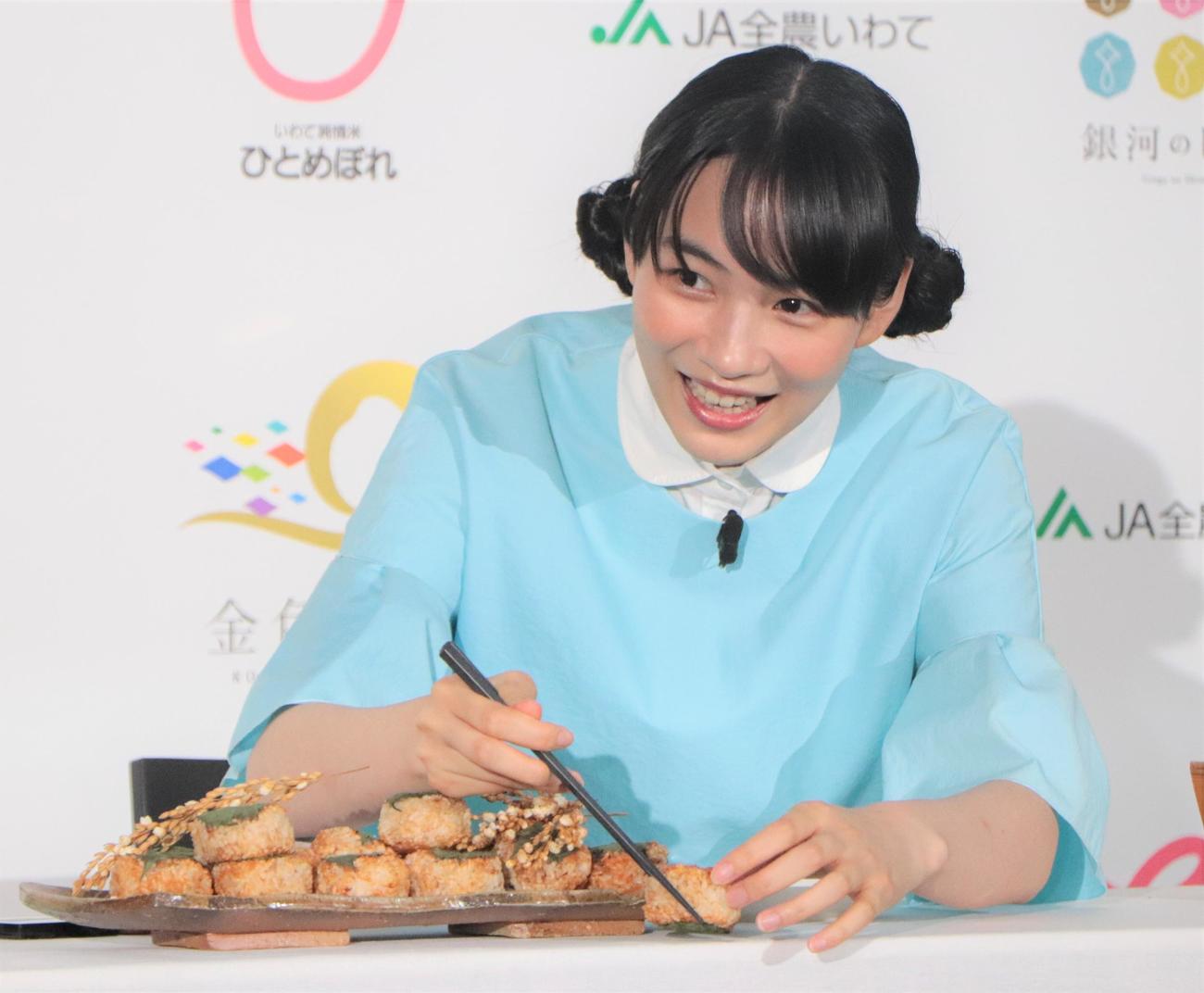 「2022『いわて純情米』新CM発表イベント」で焼きおにぎりをつかみきれず、思わず笑ってしまうのん（撮影・藤塚大輔）