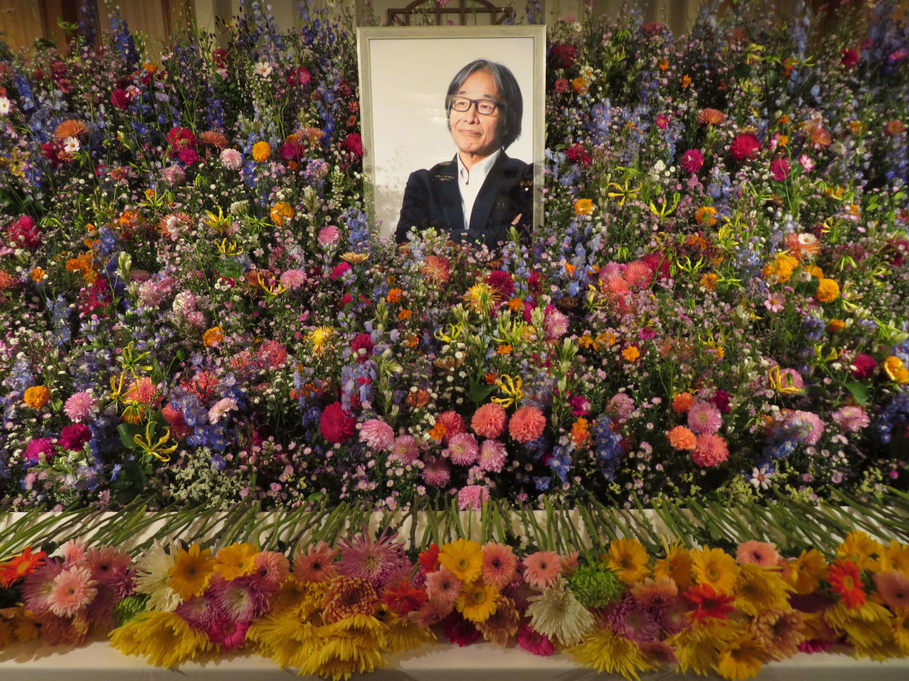 多くの花で遺影を包み込むようにしつらえられた、河村光庸さんのお別れの会の祭壇（撮影・村上幸将）