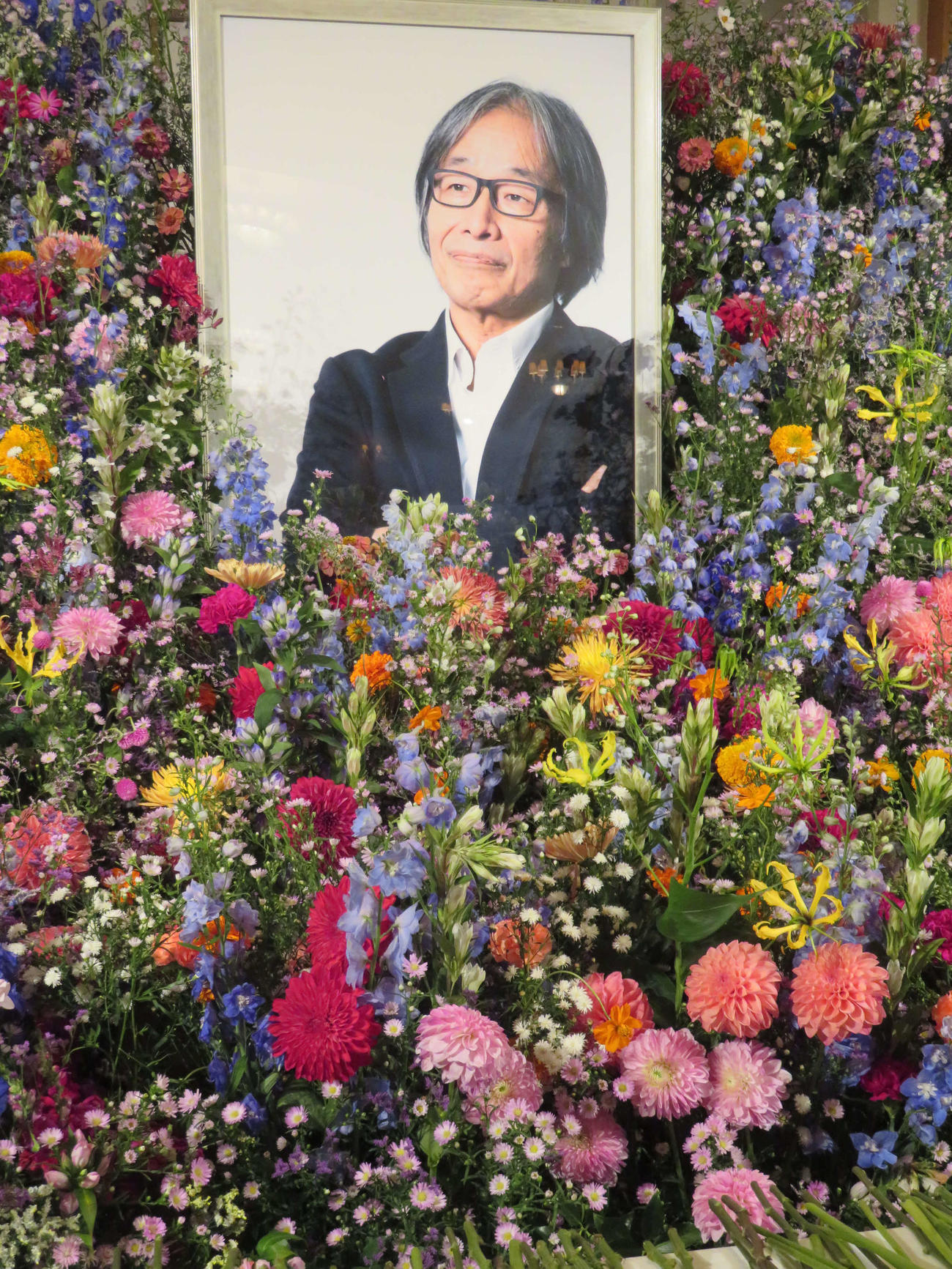 多くの花で遺影を包み込むようにしつらえられた、河村光庸さんのお別れの会の祭壇（撮影・村上幸将）