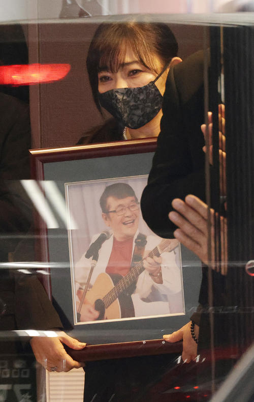 仲本工事さんの遺影を手に霊きゅう車を見送る妻の純歌さん(撮影・中島郁夫)
