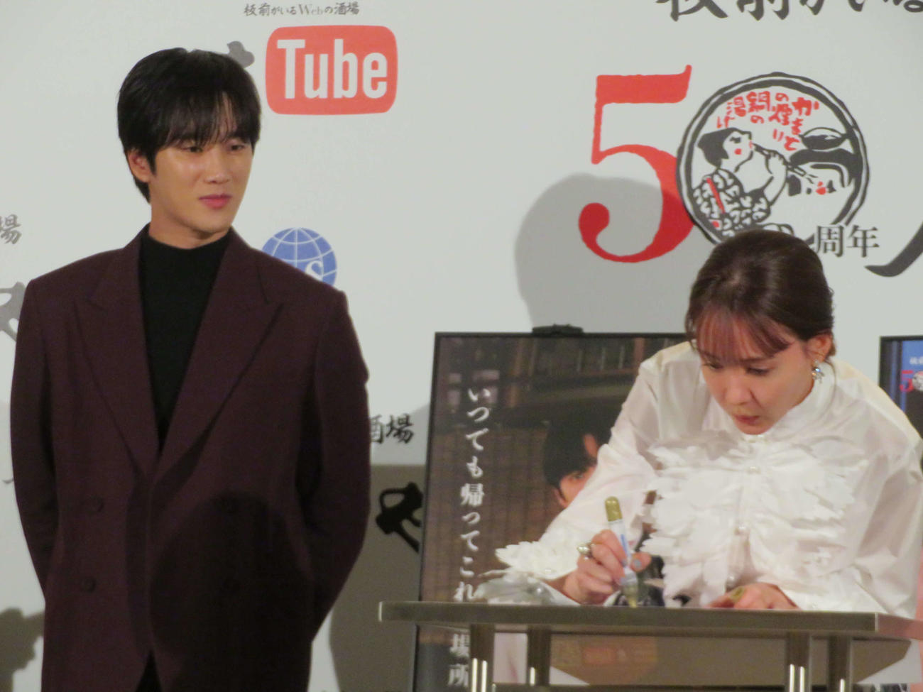 「庄や」50周年記念ドラマ「いつでも帰ってこれる場所」公開記者発表会で、ポスターにサインするトリンドル玲奈を見守るアン・ボヒョン（撮影・村上幸将）