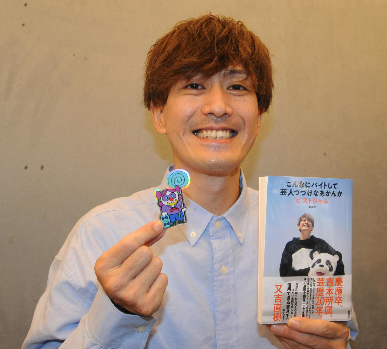 著書「こんなにバイトして芸人つづけなあかんか」を発売し、自作のアートシールと書籍を持つピストジャム（撮影・松尾幸之介）