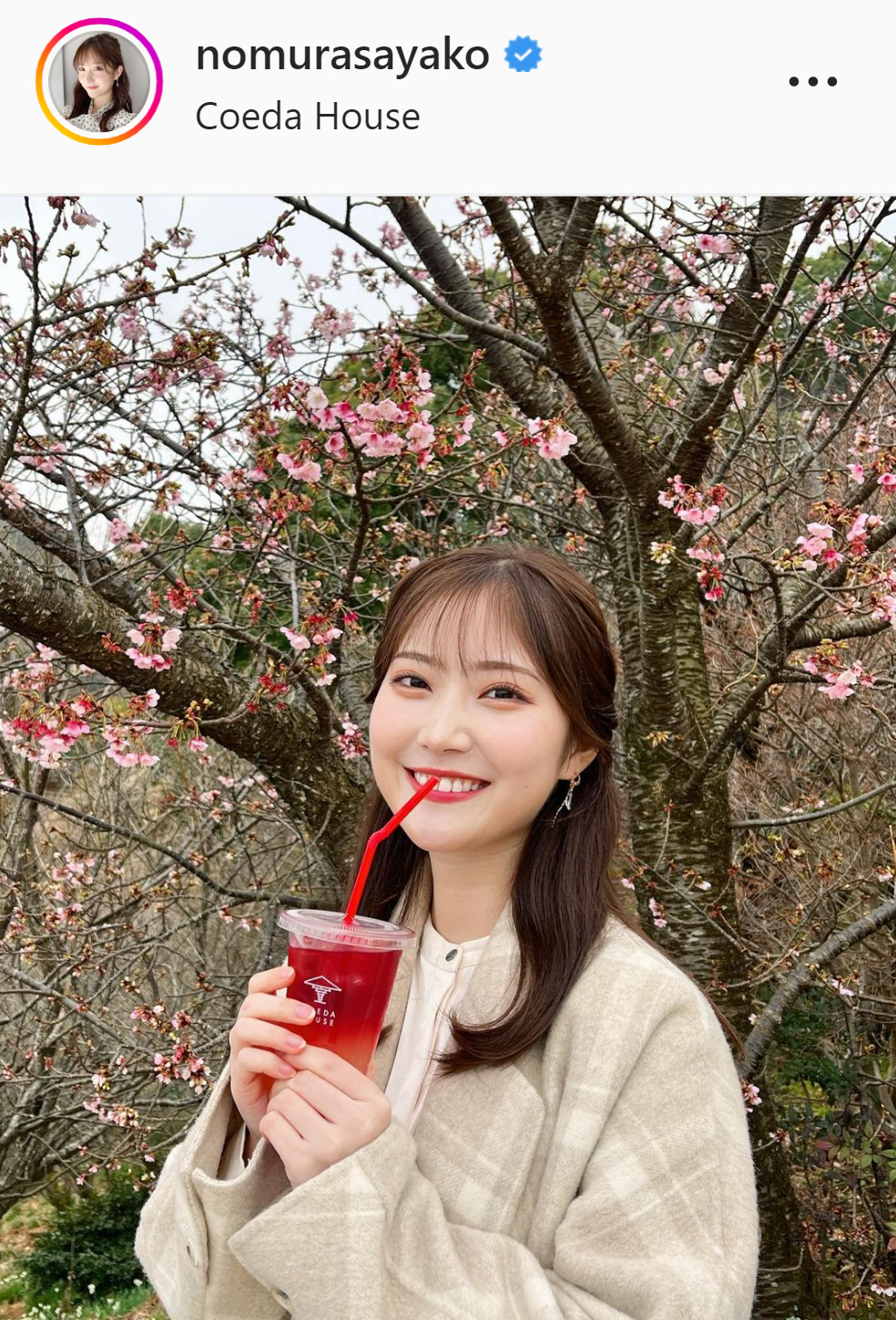 桜の前で笑顔でドリンクを飲む野村彩也子アナ（野村彩也子アナのインスタグラムより）