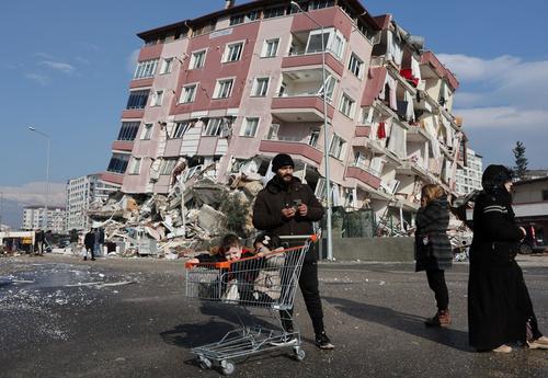 トルコ南部ハタイ県で、地震により倒壊した建物の前にたたずむ人々（ロイター）