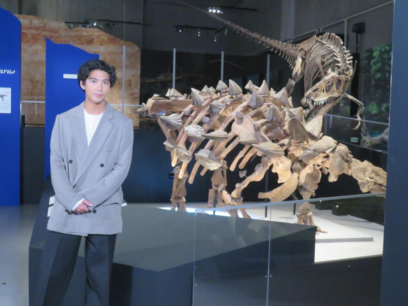 鎧竜ズールの化石の前でポーズを取る賀来賢人