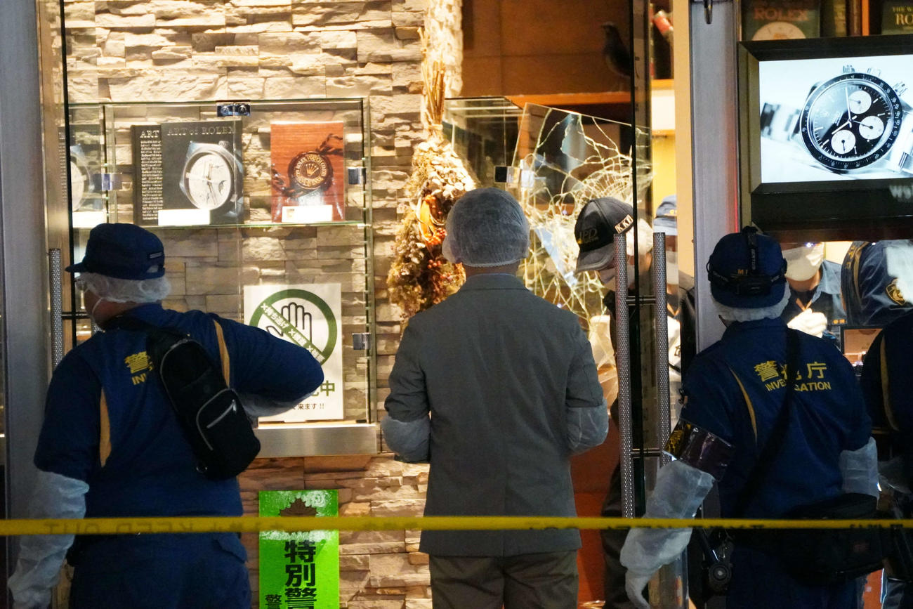 強盗が入った時計店を調べる警察官。ショーケースのガラスは破損している（撮影・沢田直人）