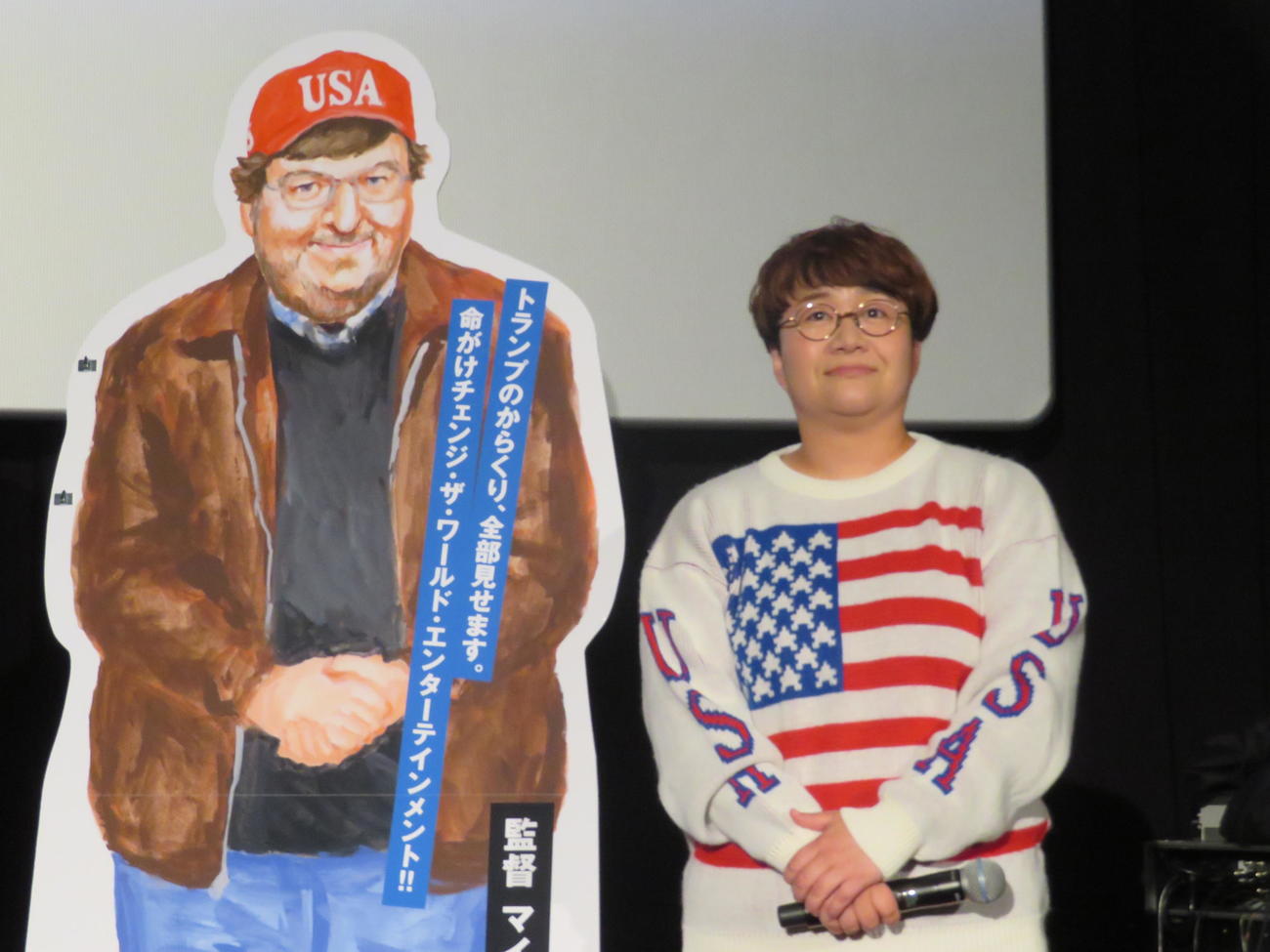 マイケル・ムーア監督の看板の横で同じポーズを取る近藤春菜（2018年11月撮影）