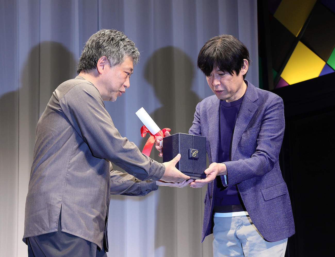 カンヌ国際映画祭「脚本賞」を受賞した坂元裕二氏（右）は是枝裕和監督からトロフィーを受け取る（撮影・足立雅史）