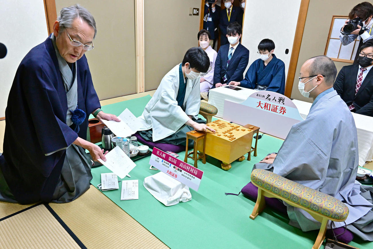 立会人の田中寅彦九段（左）が開封した封じ手を指す藤井聡太竜王（中央、右は渡辺明名人＝日本将棋連盟提供）