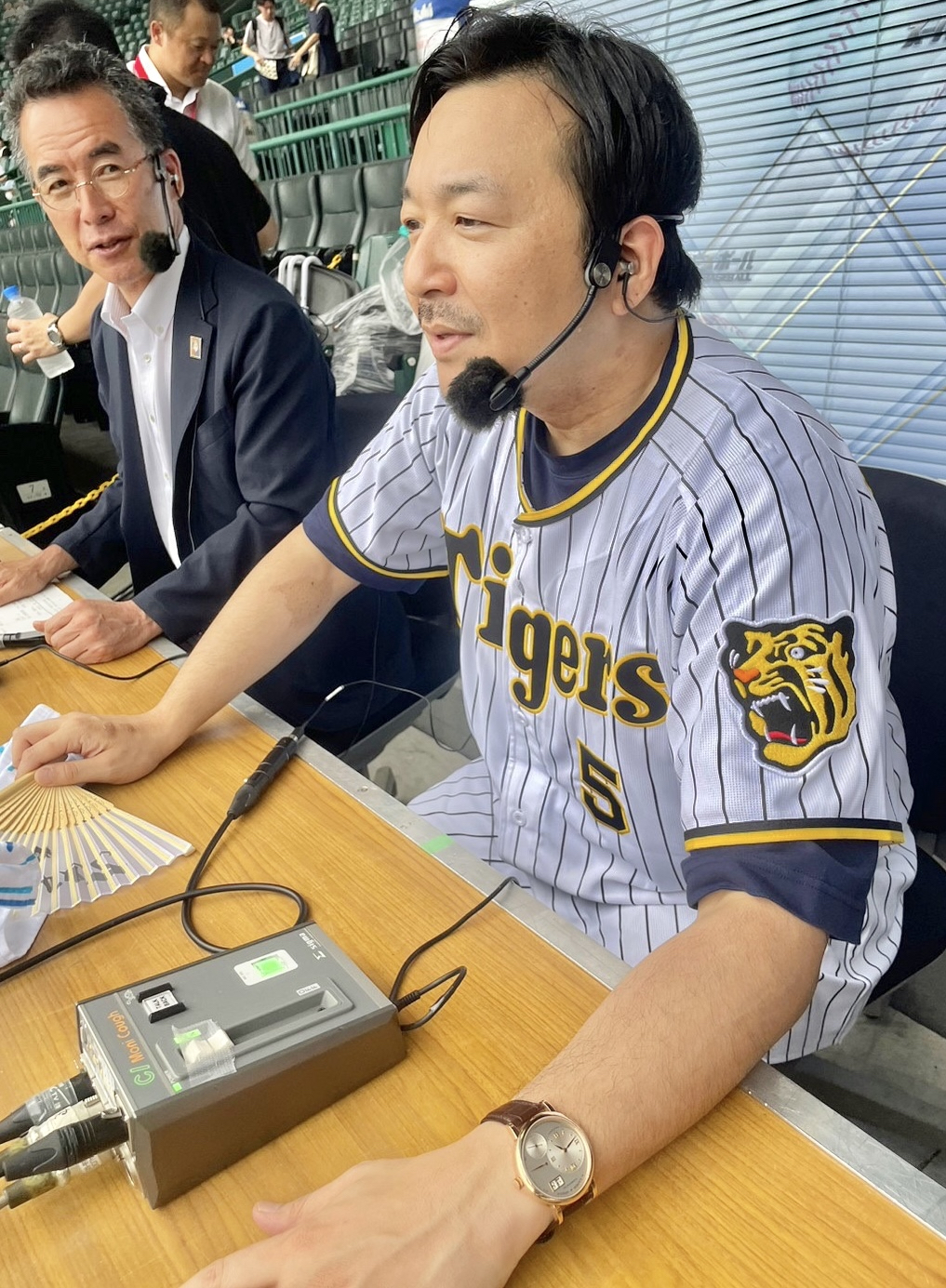 放送席で実況の伊藤史隆アナウンサー（左）の隣で食い入るように戦況を見つめる今村翔吾氏
