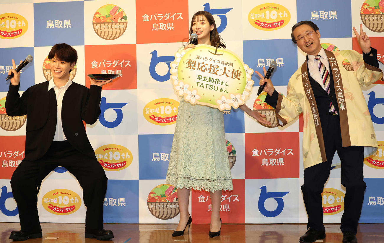 「カニ取県へようこそ！ウエルカニ！」。平井鳥取県知事（右）の発声でポーズを決めるTATSUさん（左）。中央は足立梨花（撮影・丹羽敏通）