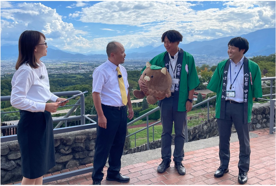 甲斐市職員（右2名）より応援アンバサダーの説明を受けるマキタスポーツ（左から2人目）