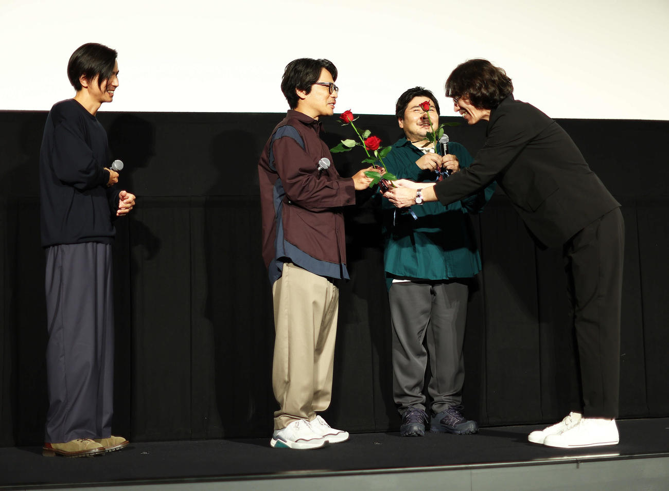 映画「くるりのえいが」完成披露上映会舞台あいさつで岸田繁(中央）らにバラの花を手渡す佐渡岳利監督（右）（撮影・河田真司）