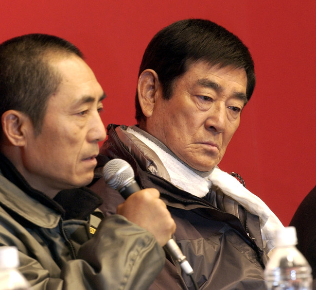 映画「千里走単騎」製作発表会見　高倉健は首にタオルを巻いた撮影時の衣装で会見する。左はチャン・イーモウ監督(05年2月）