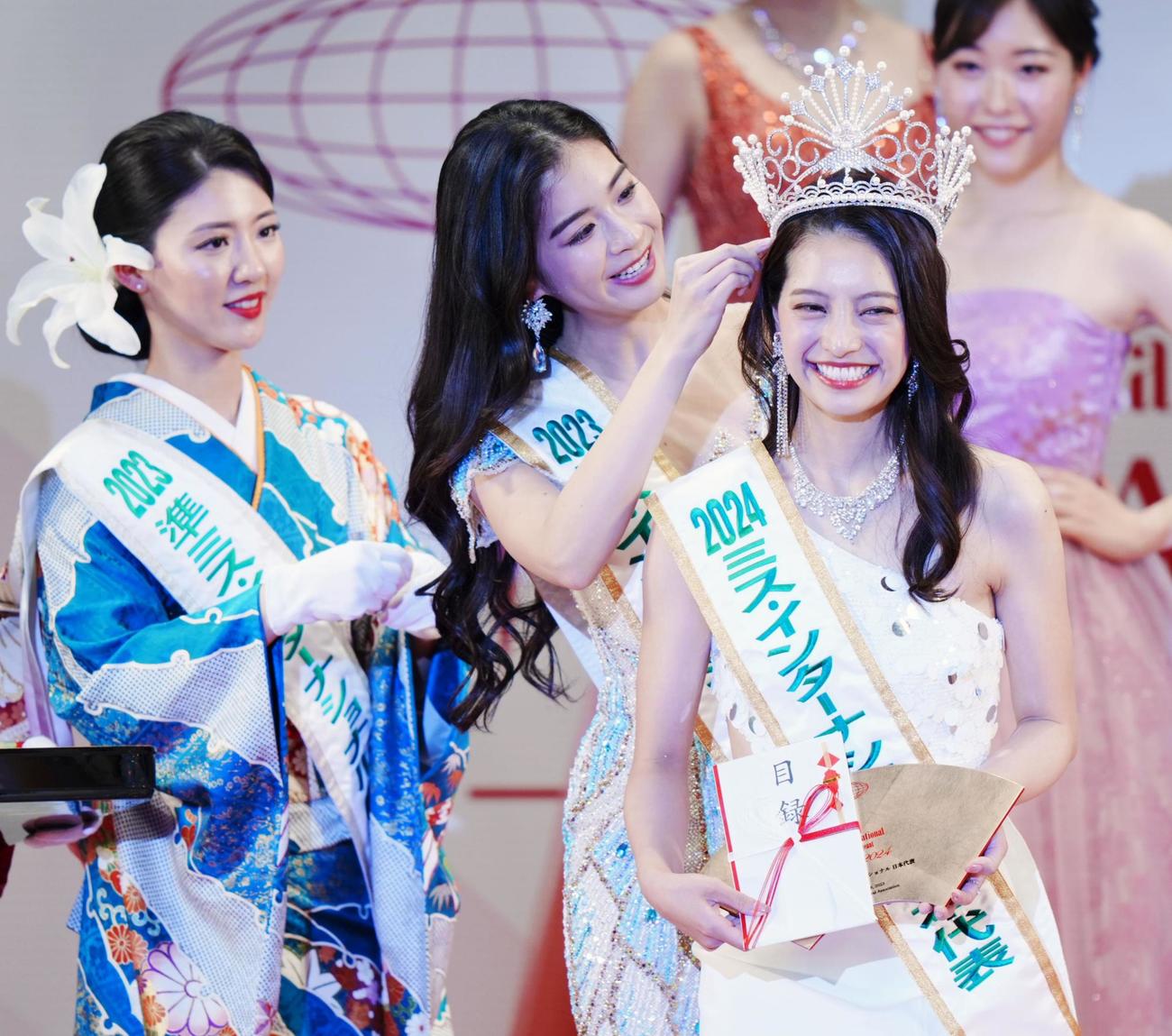 「ミス・インターナショナル世界大会2024」に出場する日本代表に選ばれ、昨年代表の米山珠央さん（中央）からティアラを着けてもらう植田明依さん（共同）