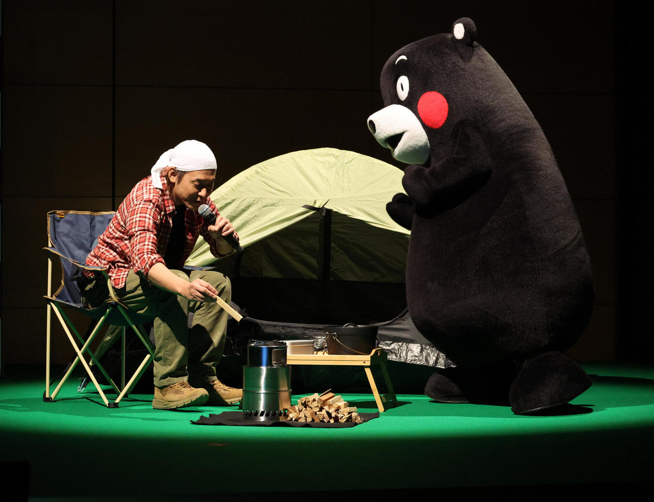 キャンプ風景を見せるヒロシ。右はくまモン（撮影・中島郁夫）