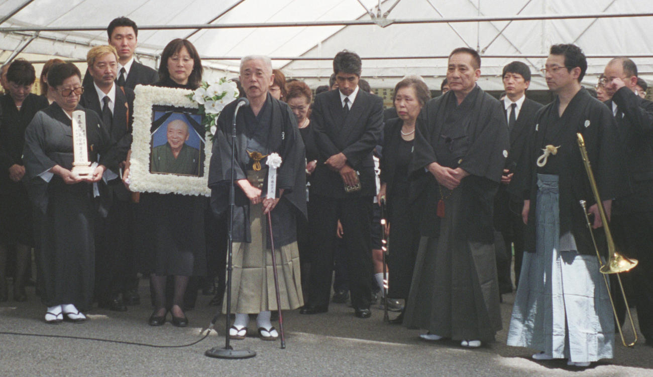 2003年6月、春風亭柳昇さん告別式　あいさつする桂文治葬儀委員長。前列左から喪主の妻孝子さん、長女順子さん、春風亭小柳枝さん、トロンボーンを持つ春風亭昇太