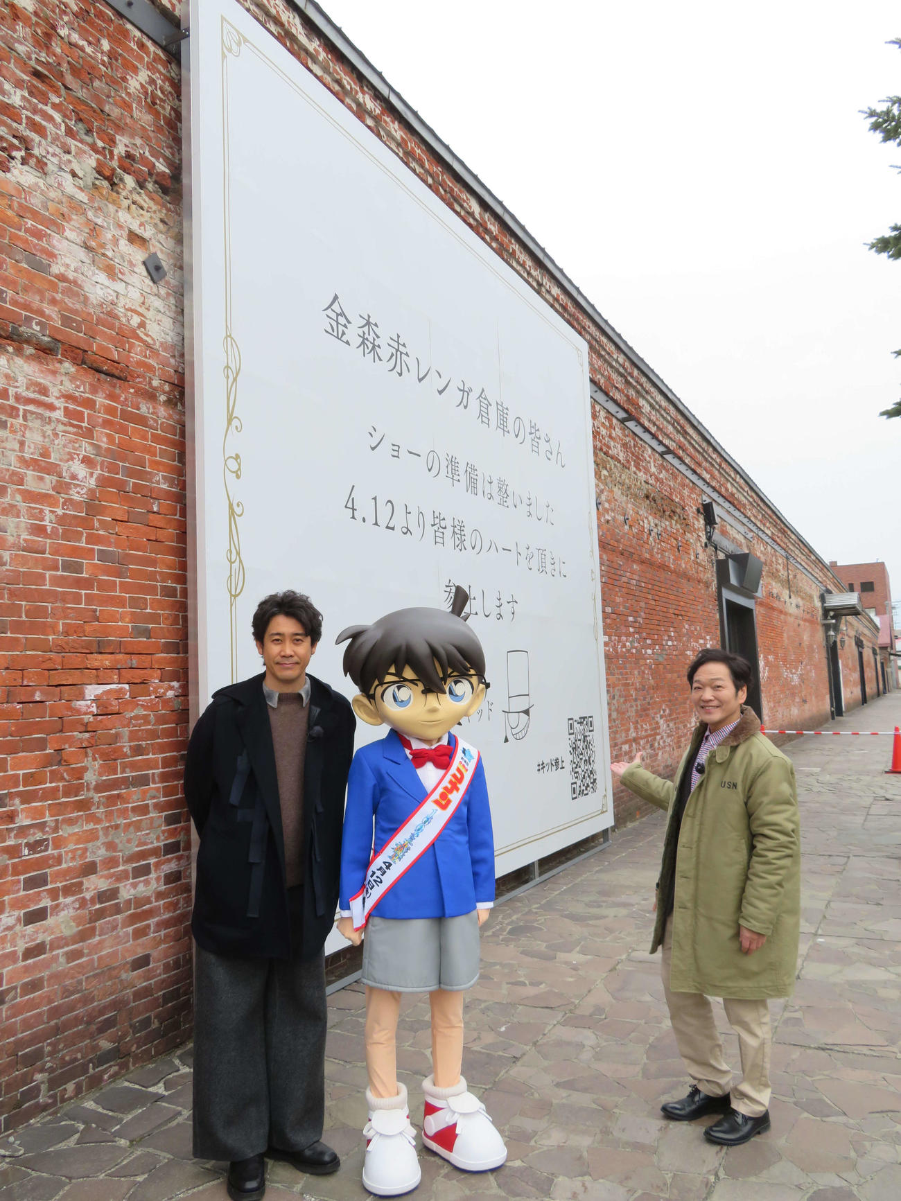 アニメ映画「名探偵コナン　100万ドルの五稜星」公開前イベントで、函館市内の金森赤レンガ倉庫街を訪れ、怪盗キッドの予告状を背に笑顔の、左から大泉洋、江戸川コナン、山口勝平（撮影・村上幸将）