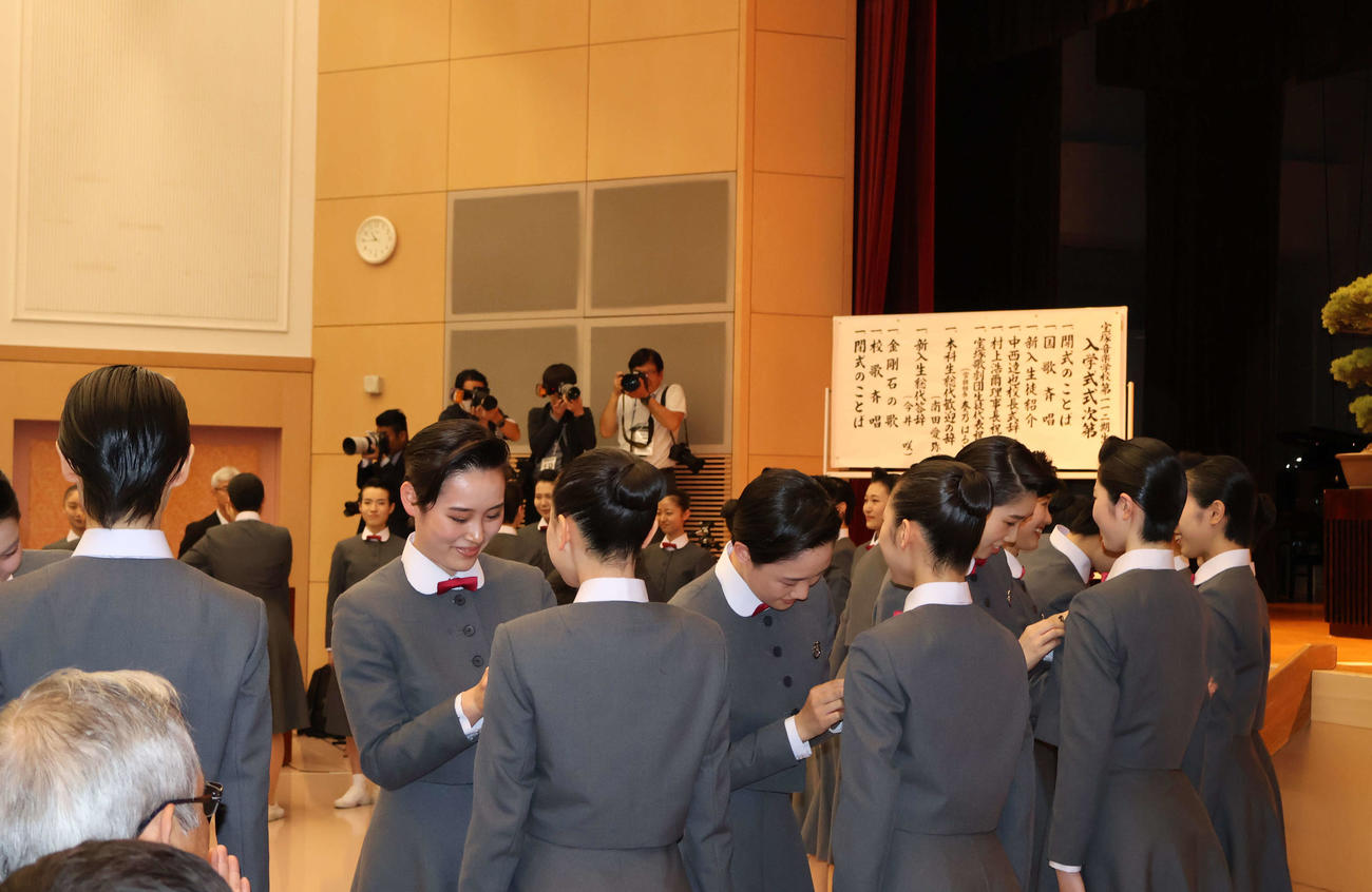 式典後、先輩になる本科生に校章を着けてもらう新入生（撮影・村上久美子）
