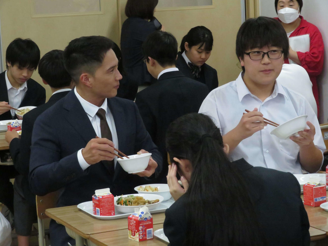 映画「おいしい給食　Road to　イカメシ」のイベントで中学校の給食の時間にサプライズ登場し、生徒と一緒に給食を食べる市原隼人