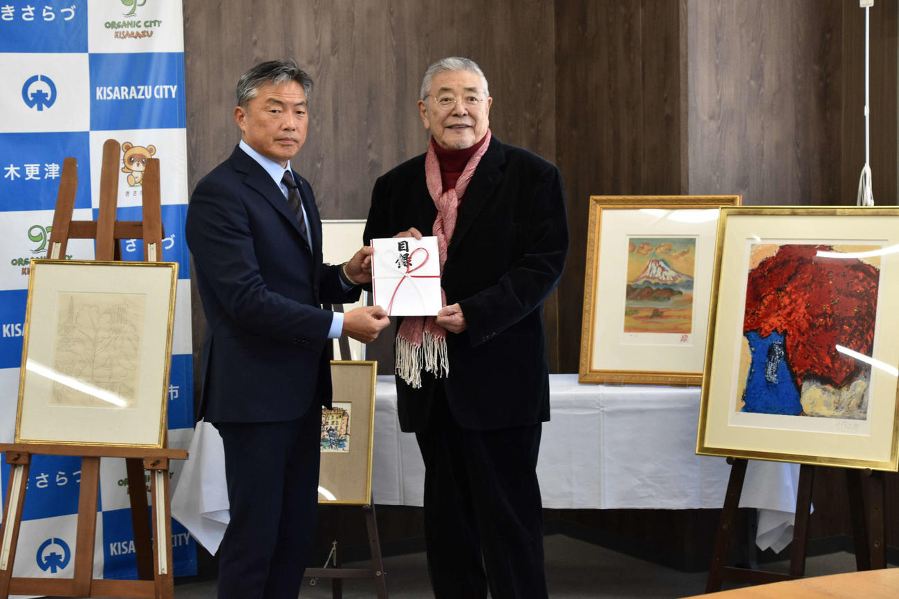 PR大使を務めた故郷の千葉県木更津市に、自身が描いた絵画を含む美術品38点を寄贈し、渡辺芳邦市長（左）に目録を手渡した中尾彬さん（木更津市提供）