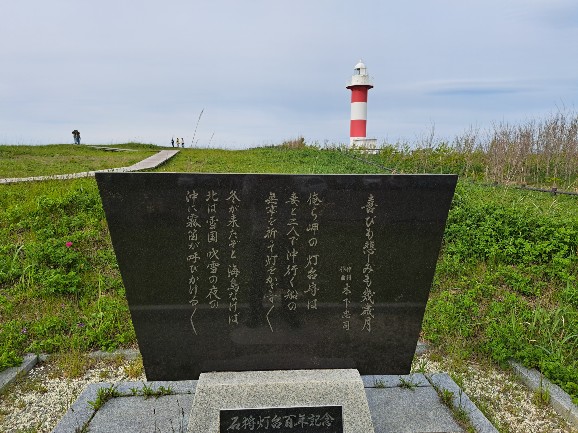 赤白しま模様の石狩灯台と「喜びも悲しみも幾歳月」の歌碑（北海道石狩市のはまなすの丘公園）