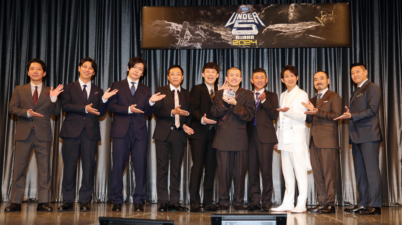 「UNDER5 AWARD 2024」で優勝した清川雄司（中央）。後方左からMCのニューヨーク嶋佐和也、屋敷裕政、審査員のマヂカルラブリー・野田クリスタル、ナイツ・塙宣之、佐久間一行、笑い飯・哲夫、NON STYLE・石田明、かもめんたる・う大、チョコレートプラネット・長田庄平（撮影・野上伸悟）