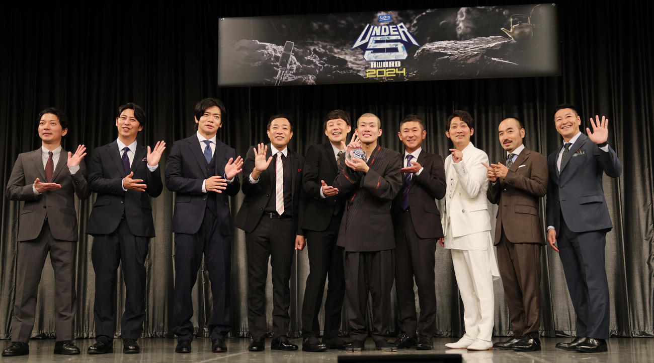「UNDER5 AWARD 2024」で優勝した清川雄司（中央）。後方左からMCのニューヨーク嶋佐和也、屋敷裕政、審査員のマヂカルラブリー・野田クリスタル、ナイツ・塙宣之、佐久間一行、笑い飯・哲夫、NON STYLE・石田明、かもめんたる・う大、チョコレートプラネット・長田庄平（撮影・野上伸悟）